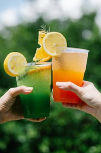 Two vibrant citrus cocktails with lemon and pineapple garnishes outdoors.